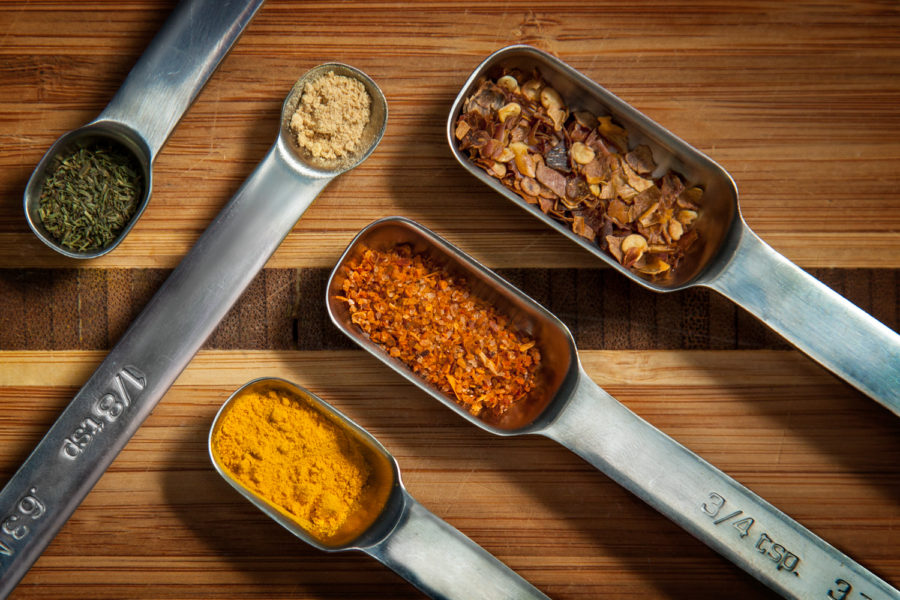 metal measuring spoons with spices on wooden board flat lay curry basil ginger chili flakes food by Teresa Ste-Marie Montreal commercial photographer ; Visual Media Strategy